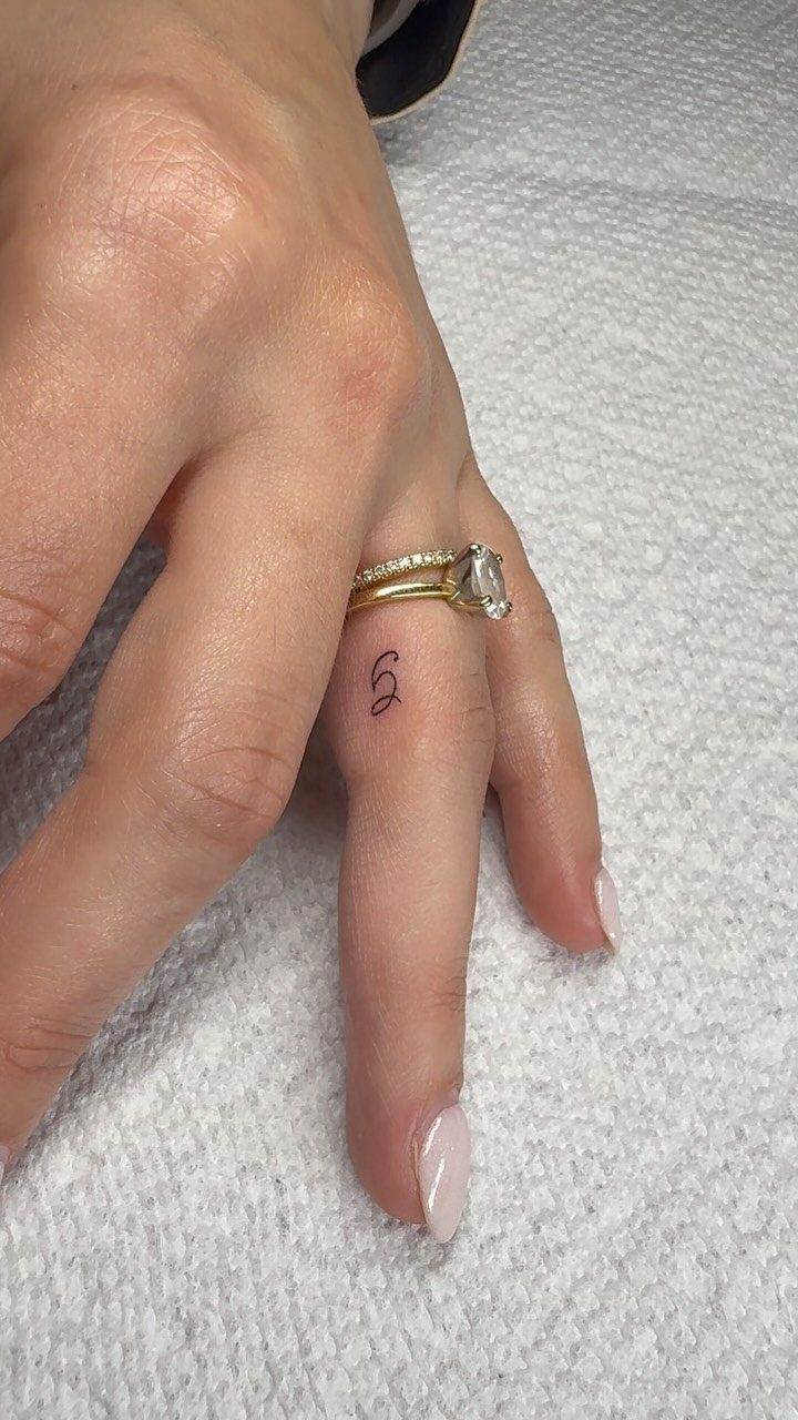Hand with a diamond ring and a small letter S initial tattoo.