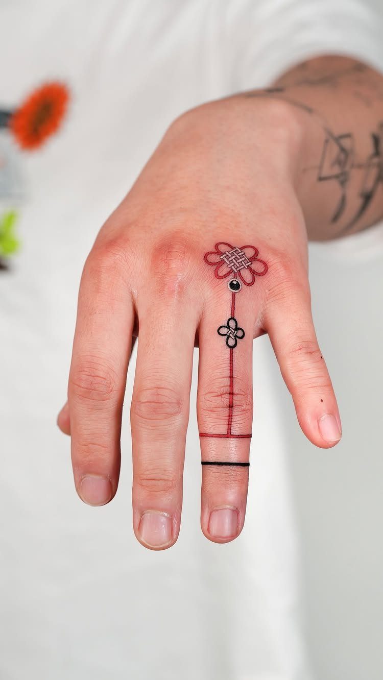 Hand with a red and black ornamental ring tattoo on the ring finger.