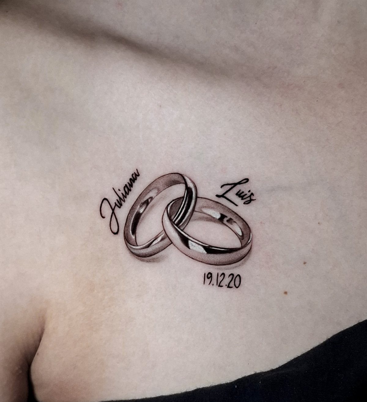 Two interlocking silver wedding ring tattoos with names and a date on skin.