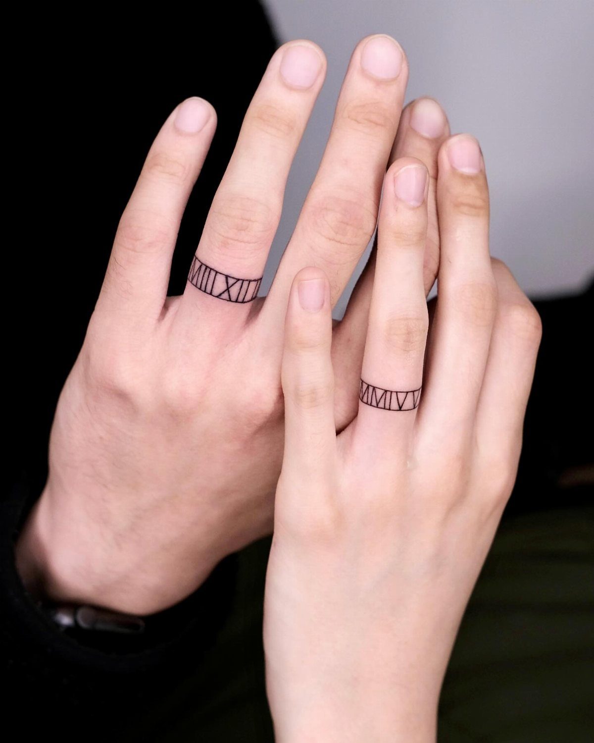 Two ring fingers with black Roman numeral tattoos wrapped around them.