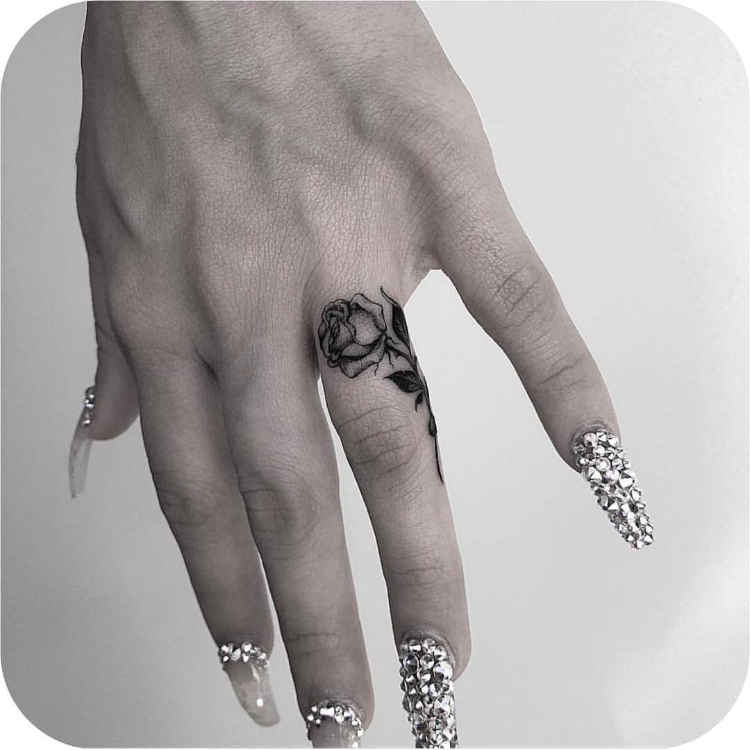 Rose tattoo wrapped around a finger with long rhinestone nails.