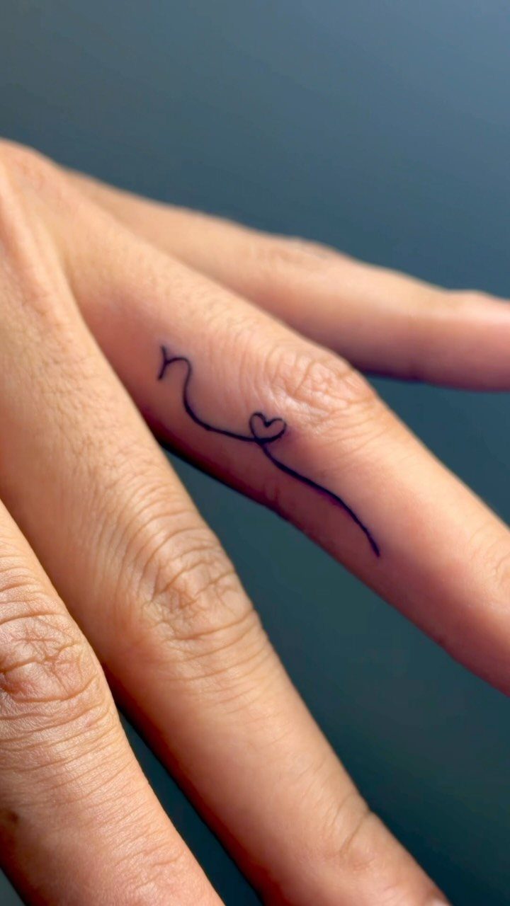 Fine line ring tattoo with a small heart on a person's finger.