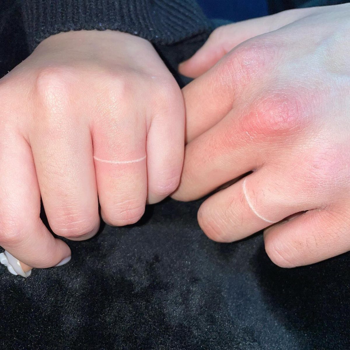 White ink ring tattoos on the fingers of two people against a dark background.