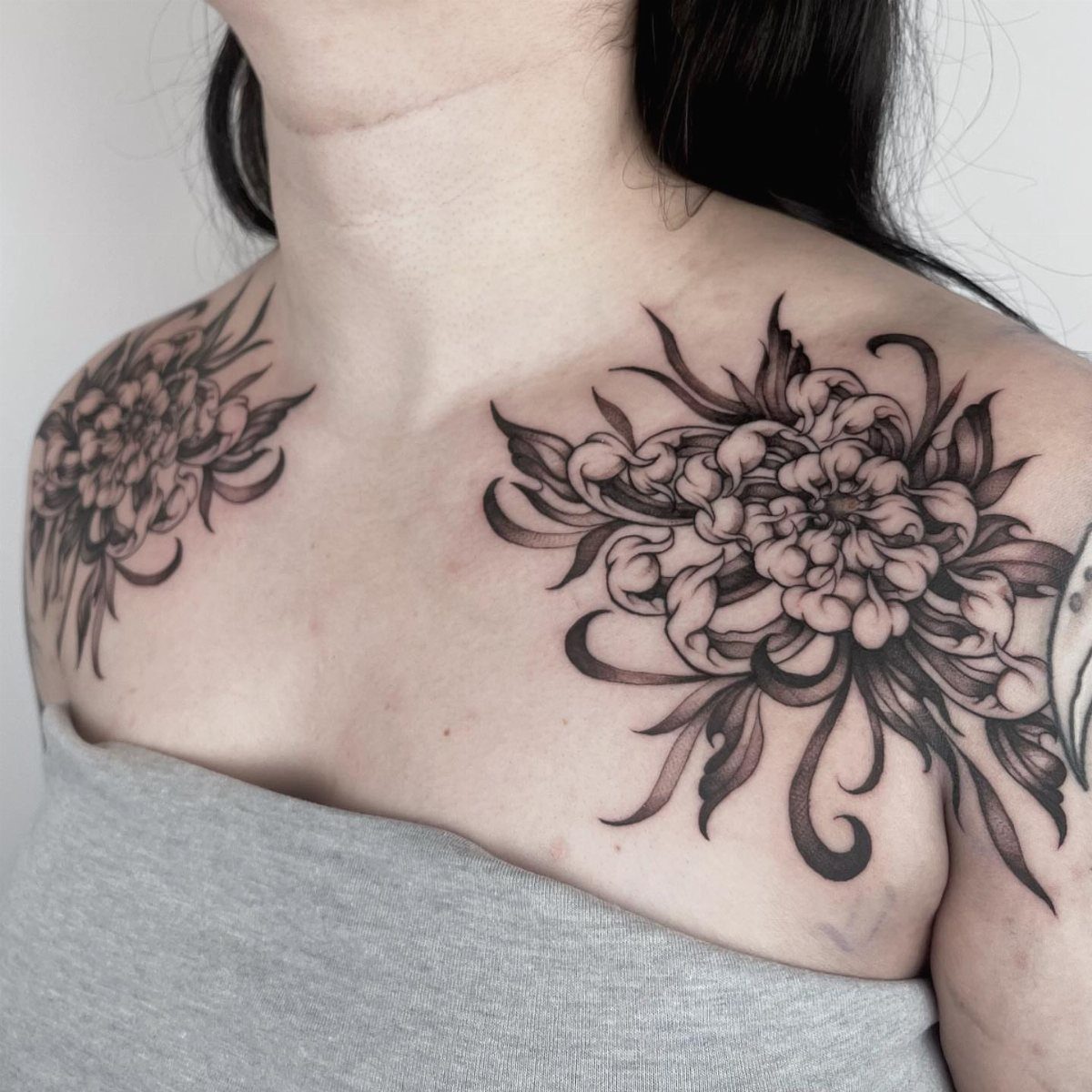 Bold blackwork flower cluster tattoos on the shoulders of a woman.