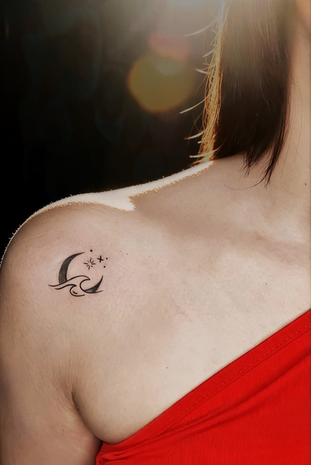 Crescent moon tattoo with a wave and stars on a woman's shoulder