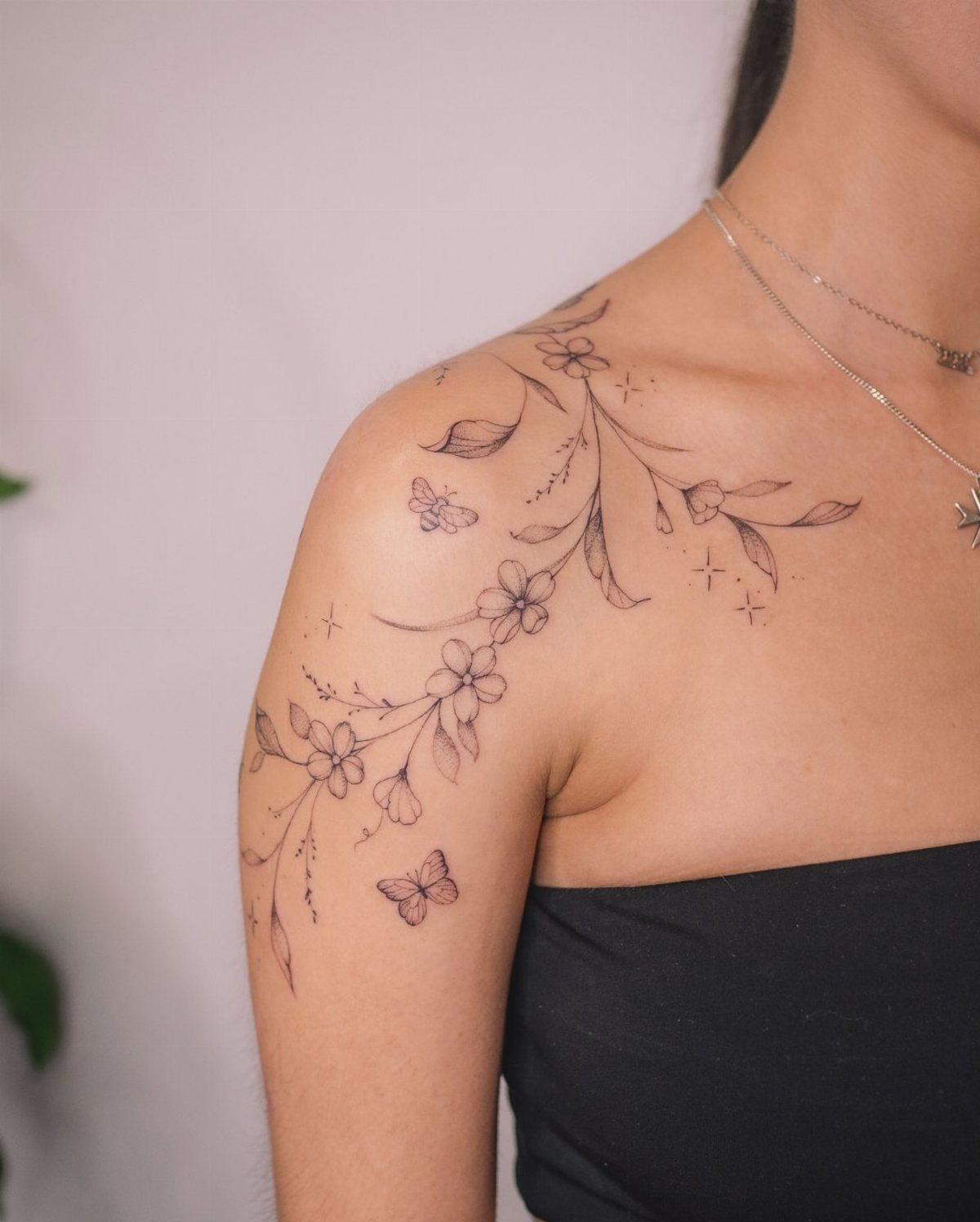 Botanical vine tattoo with small flowers and stars on a woman's shoulder