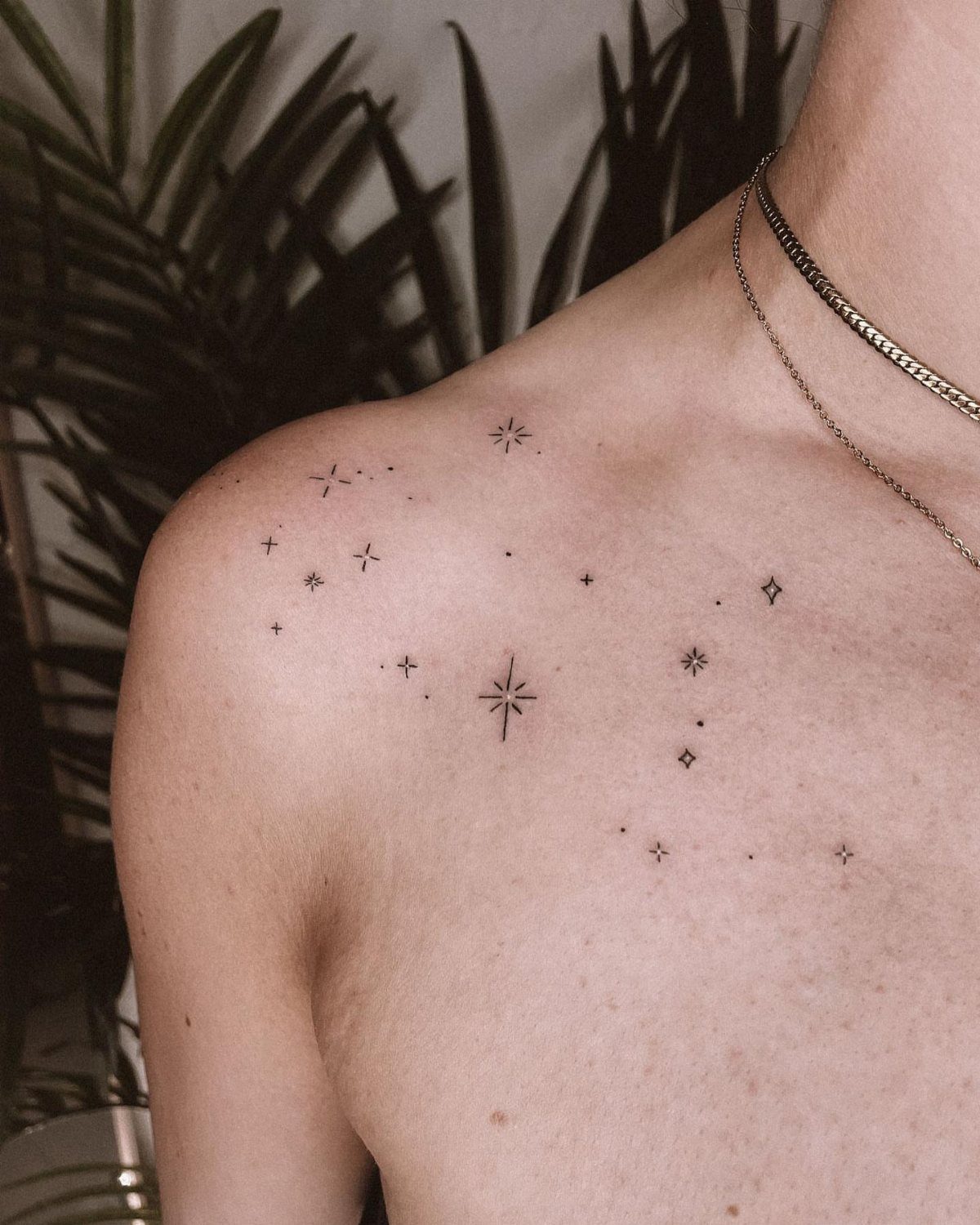 Small star and dot constellation tattoos on a person's shoulder and collarbone area