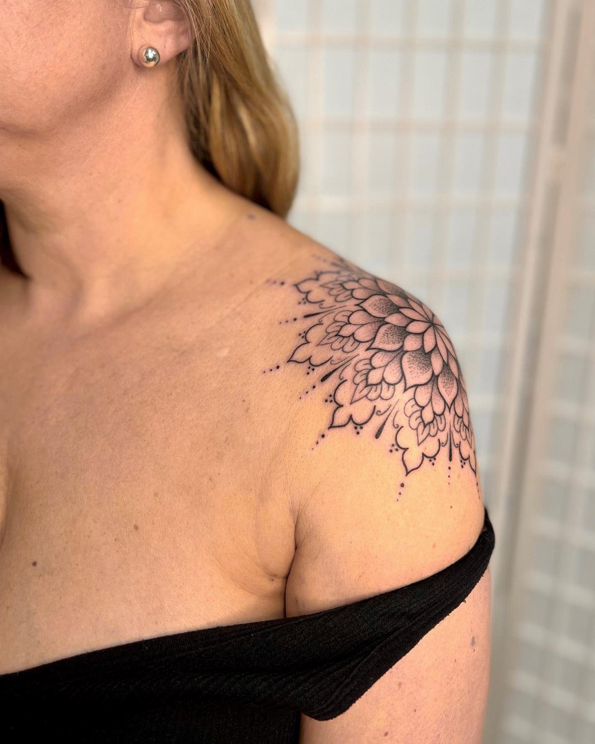 Woman's shoulder with a detailed black ink half mandala tattoo design.