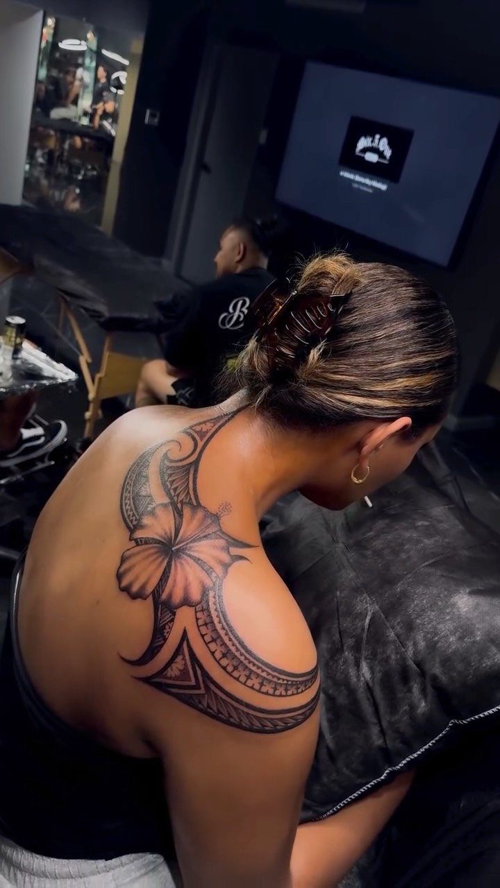 Woman with a large hibiscus and tribal tattoo on her shoulder and upper back.