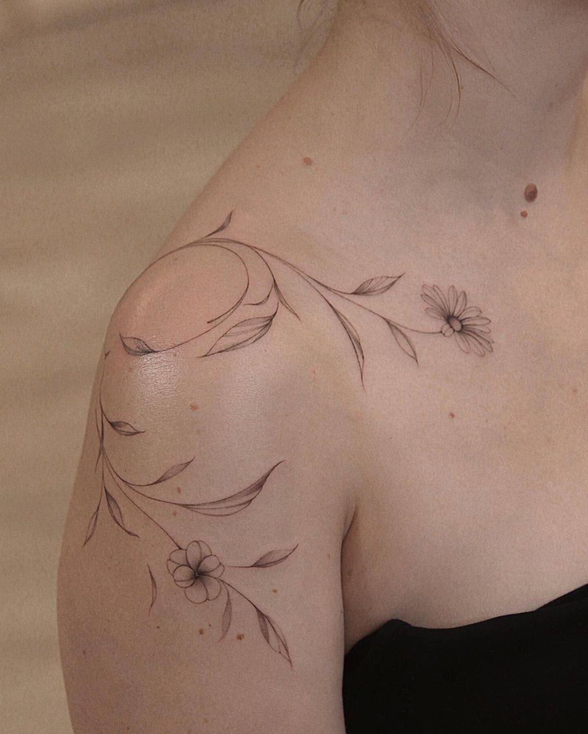 Botanical vine tattoo with leaves and flowers on a woman's shoulder.