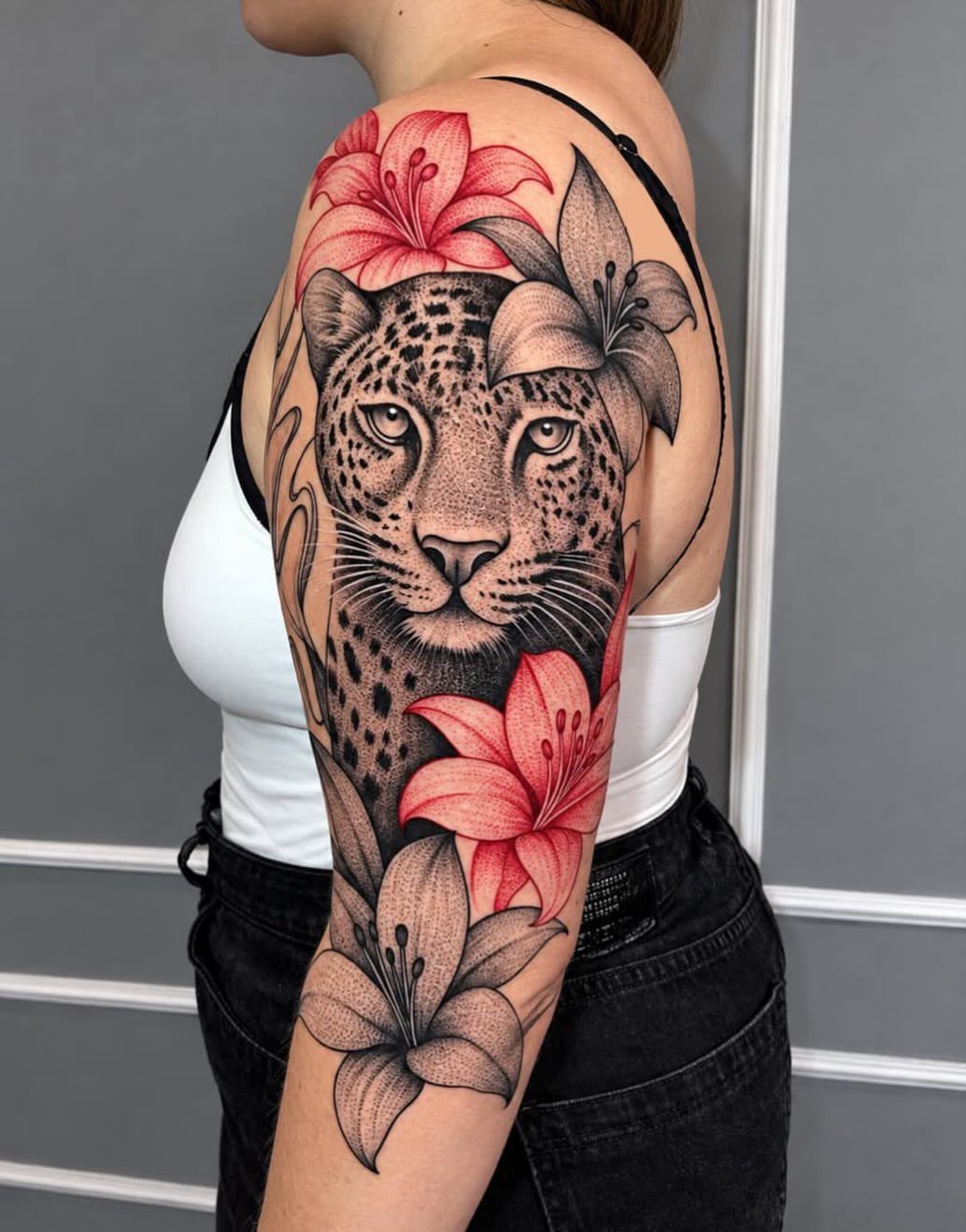 Leopard face tattoo with red and grey lilies on a woman's shoulder