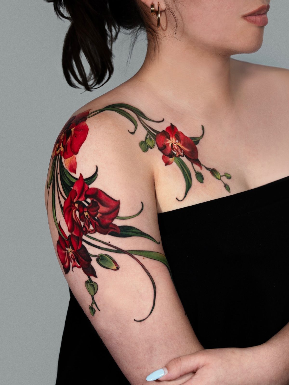 Red orchid tattoo with flowing green vines wrapping around a woman's shoulder