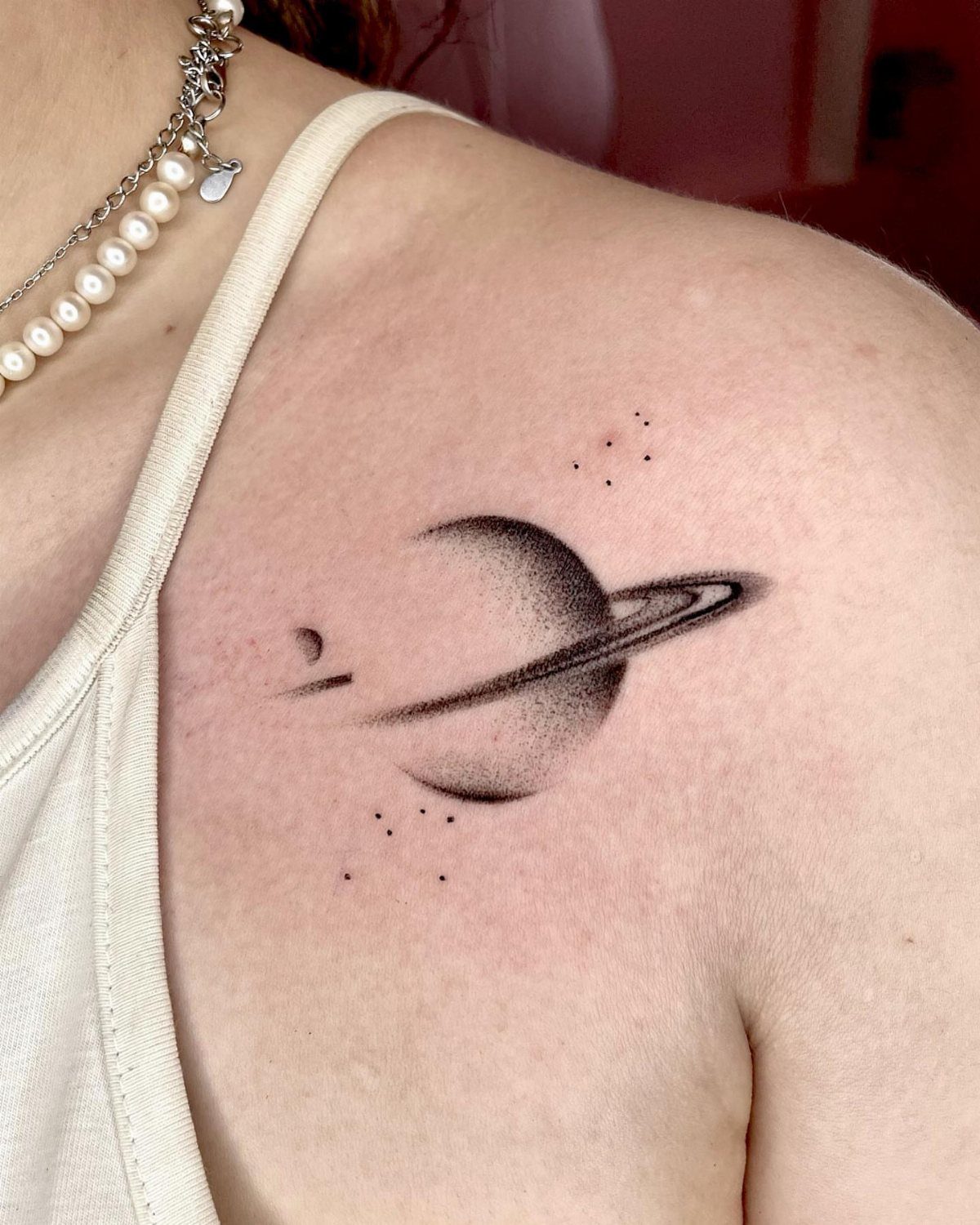 Planet with ring tattoo on a woman's shoulder with small surrounding dots