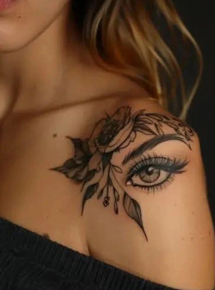 Woman's shoulder with a black ink tattoo of an eye and flowers.