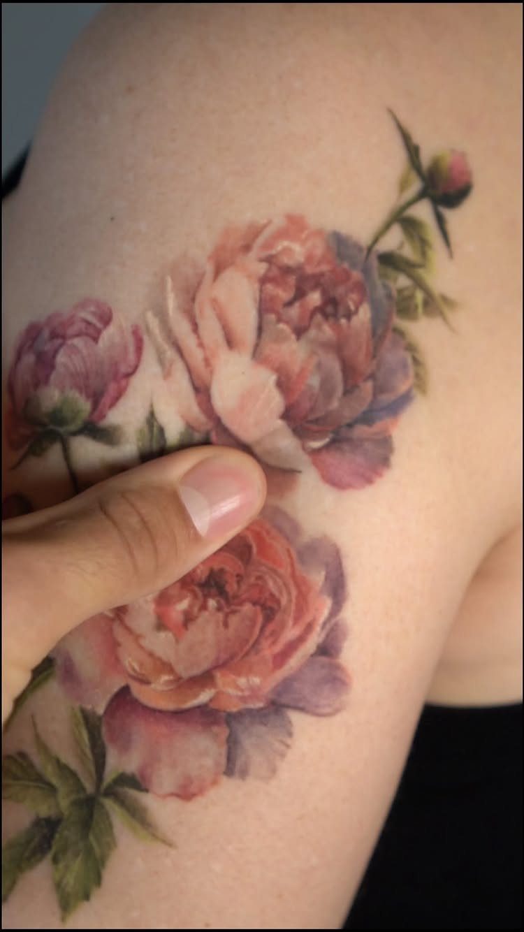 Floral peony tattoo in pink and peach tones on a person's shoulder.