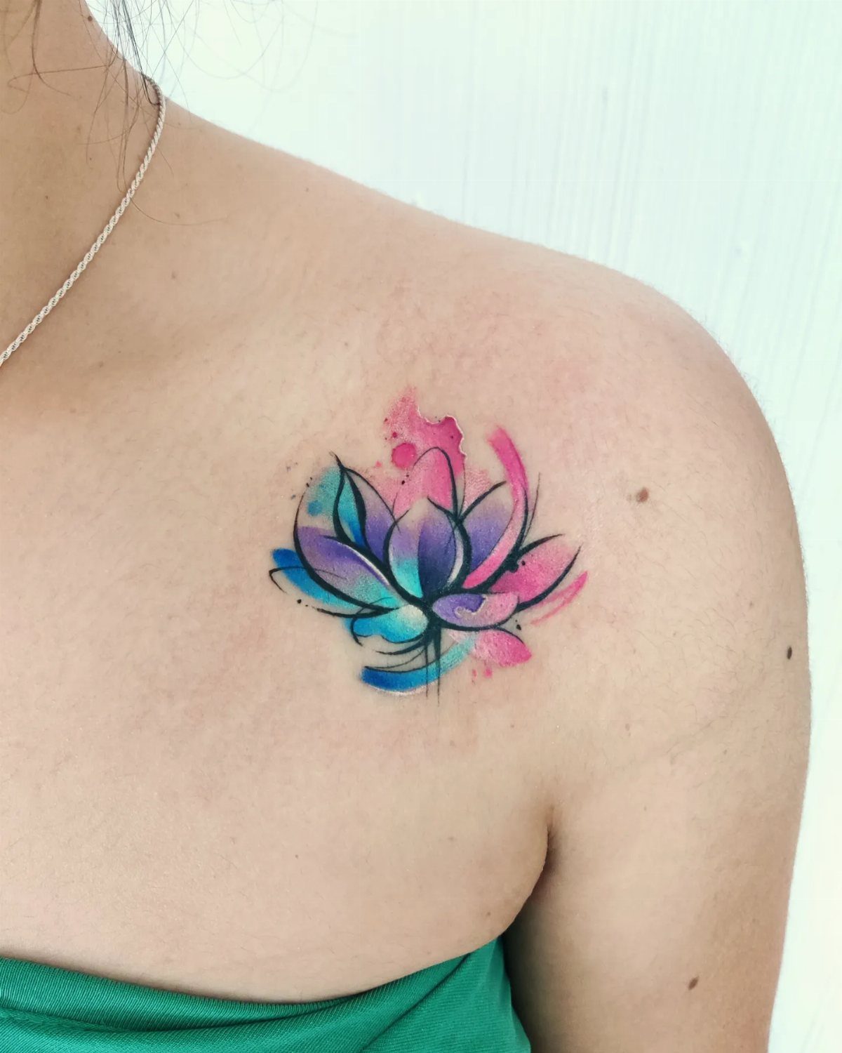 Watercolor lotus flower tattoo in blue and pink on a woman's shoulder