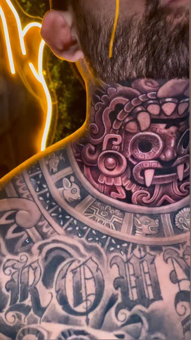 Aztec face tattoo on a man's neck with gothic lettering on chest