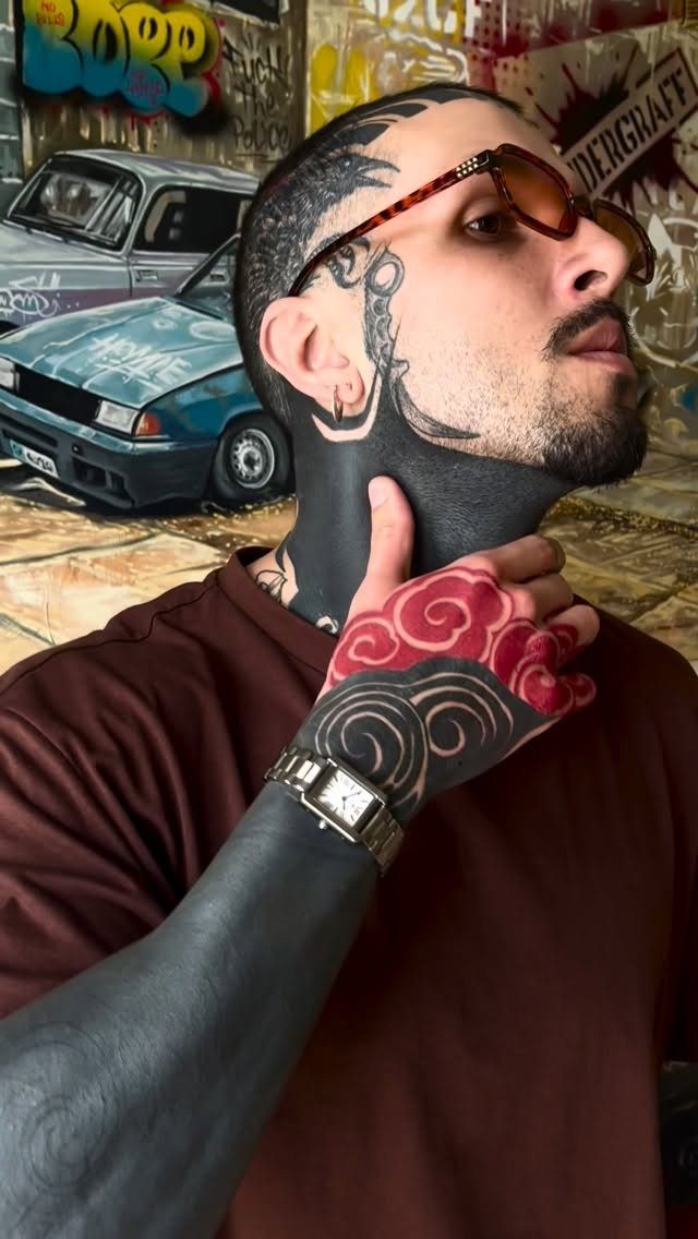 Man with solid black blackout neck tattoo and colorful hand tattoos posing outdoors.