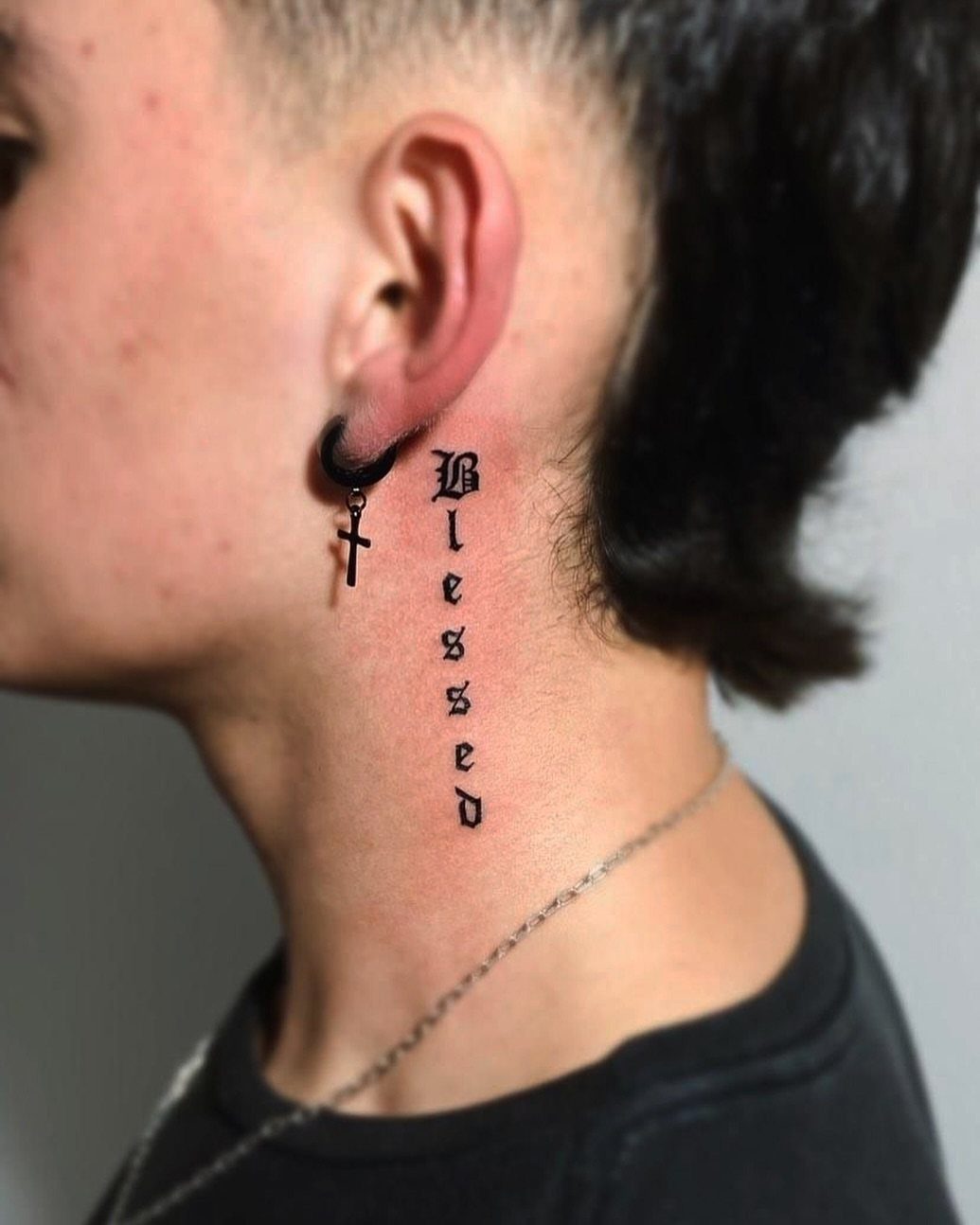 Side neck tattoo with the word Blessed in black Gothic script lettering.