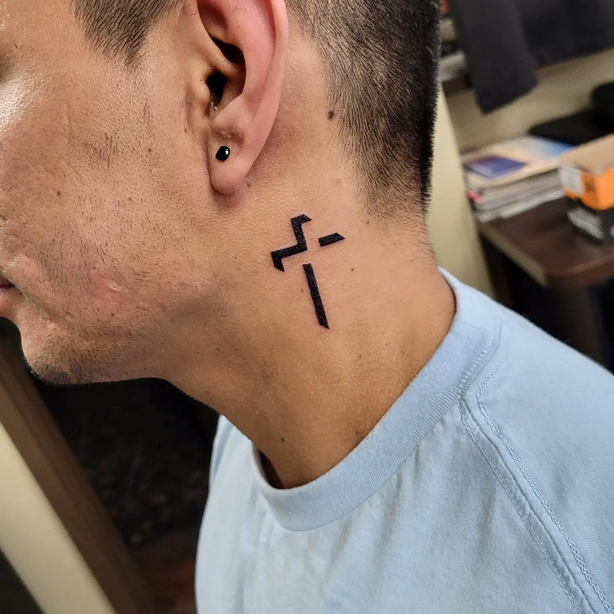 Small black cross tattoo on the side of a man's neck.