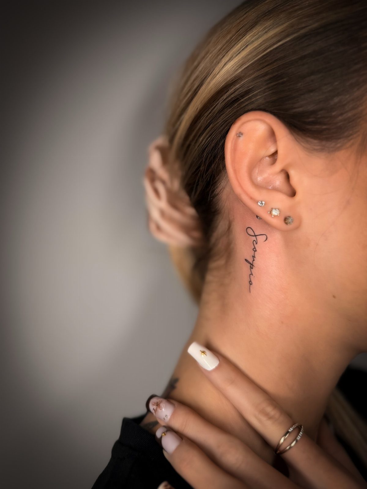Side neck with a fine line script tattoo and ear piercings.