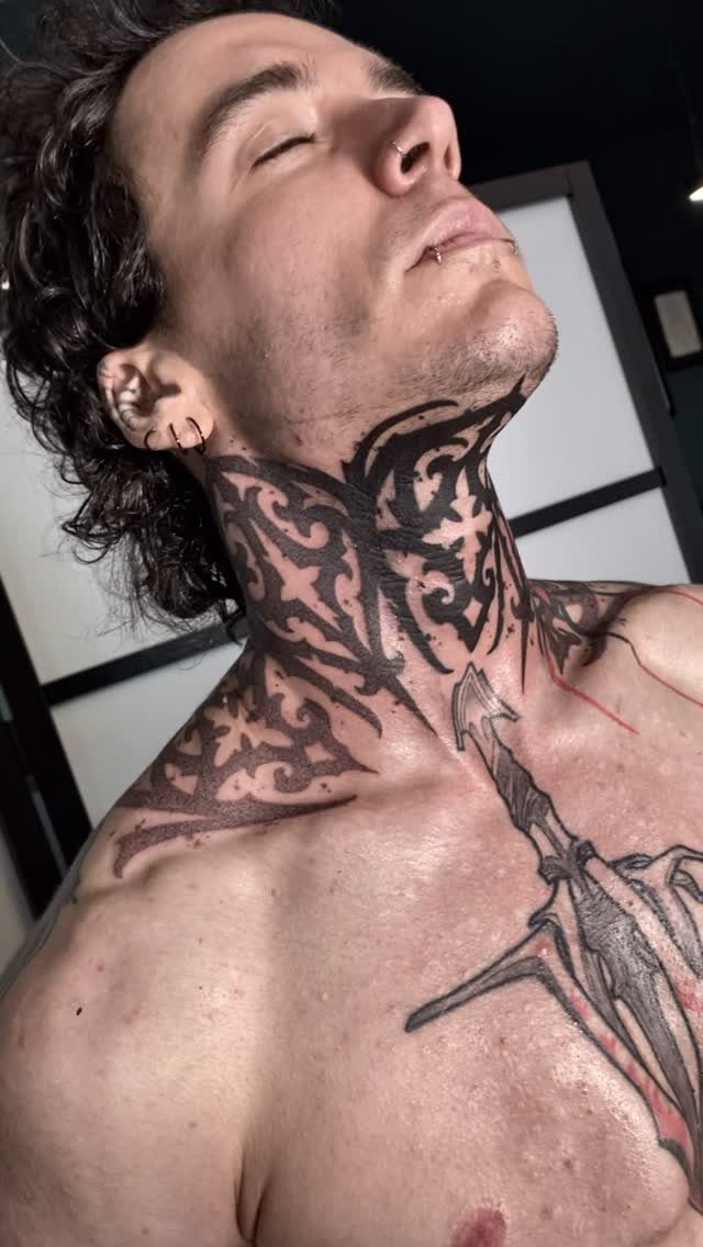 Man with bold black gothic swirling tattoos on his neck and chest.