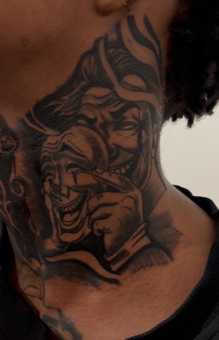 Black and grey tattoo on a side neck depicting a smiling man with a mask.