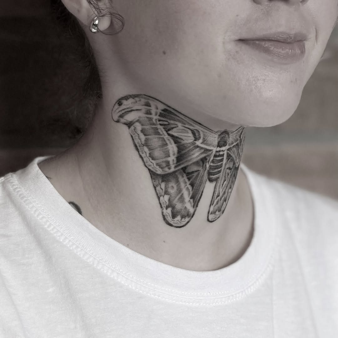 Moth tattoo on the side of a person's neck in black and white.