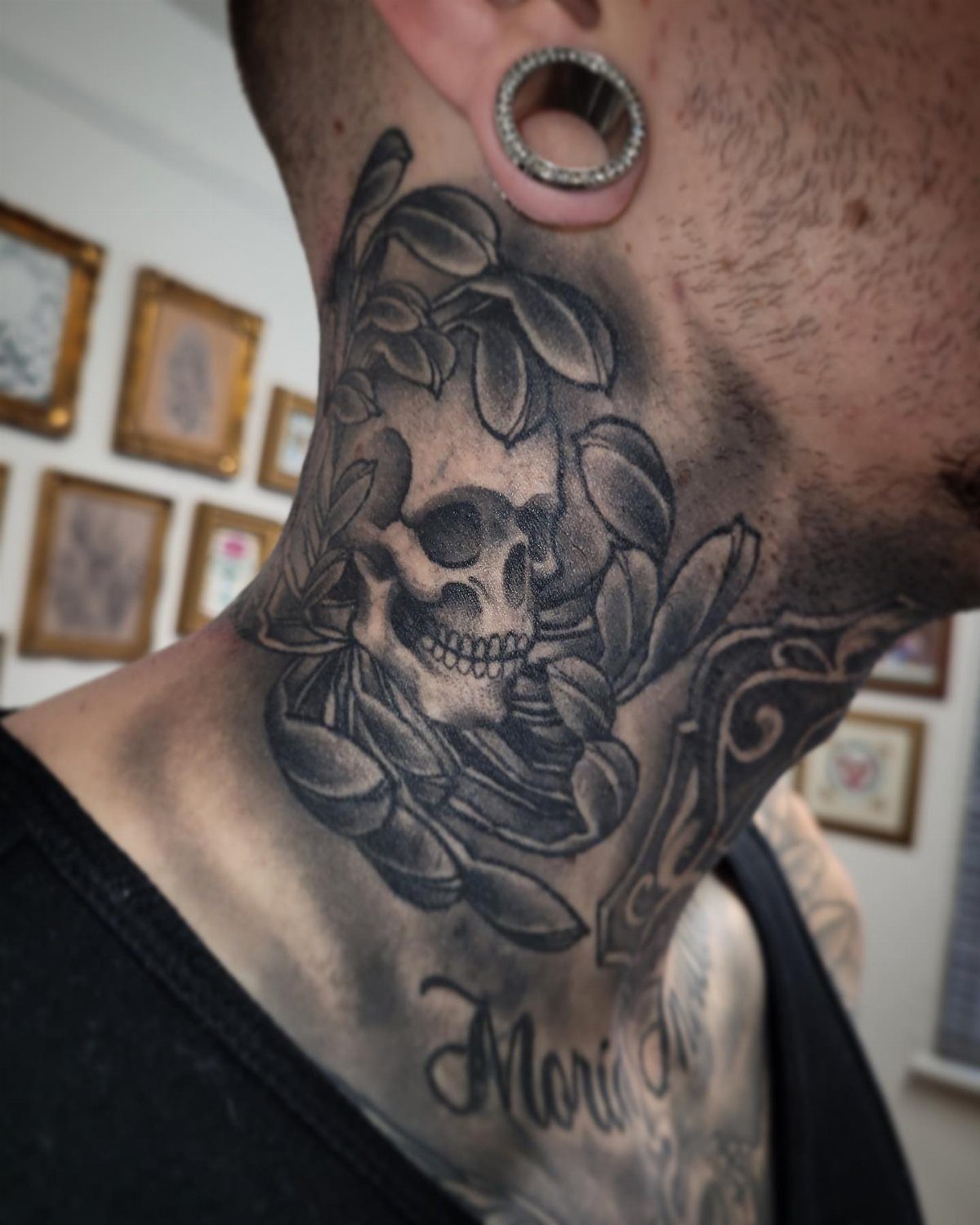 Skull tattoo on a person's neck surrounded by decorative leaves and shading.