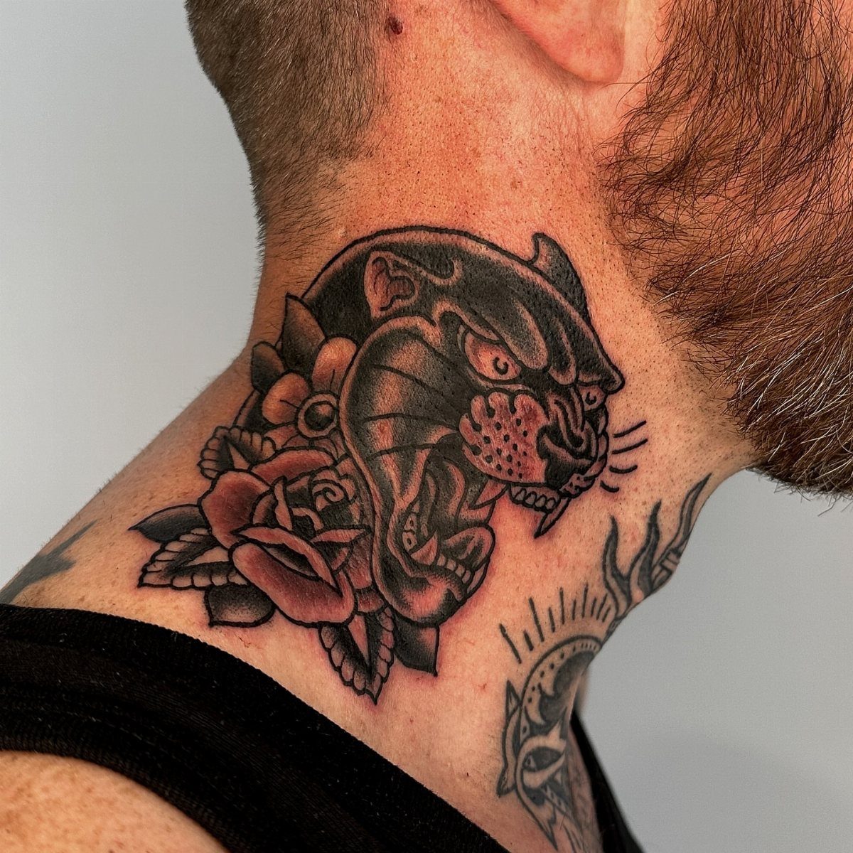 Traditional black panther head tattoo with red roses on a person's side neck.