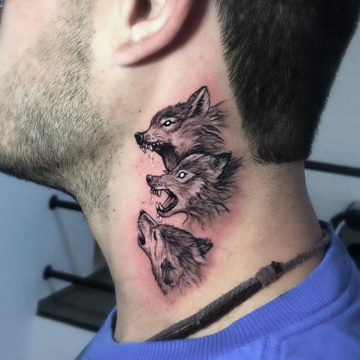 Three howling wolf heads tattooed in black and grey on a man's side neck.