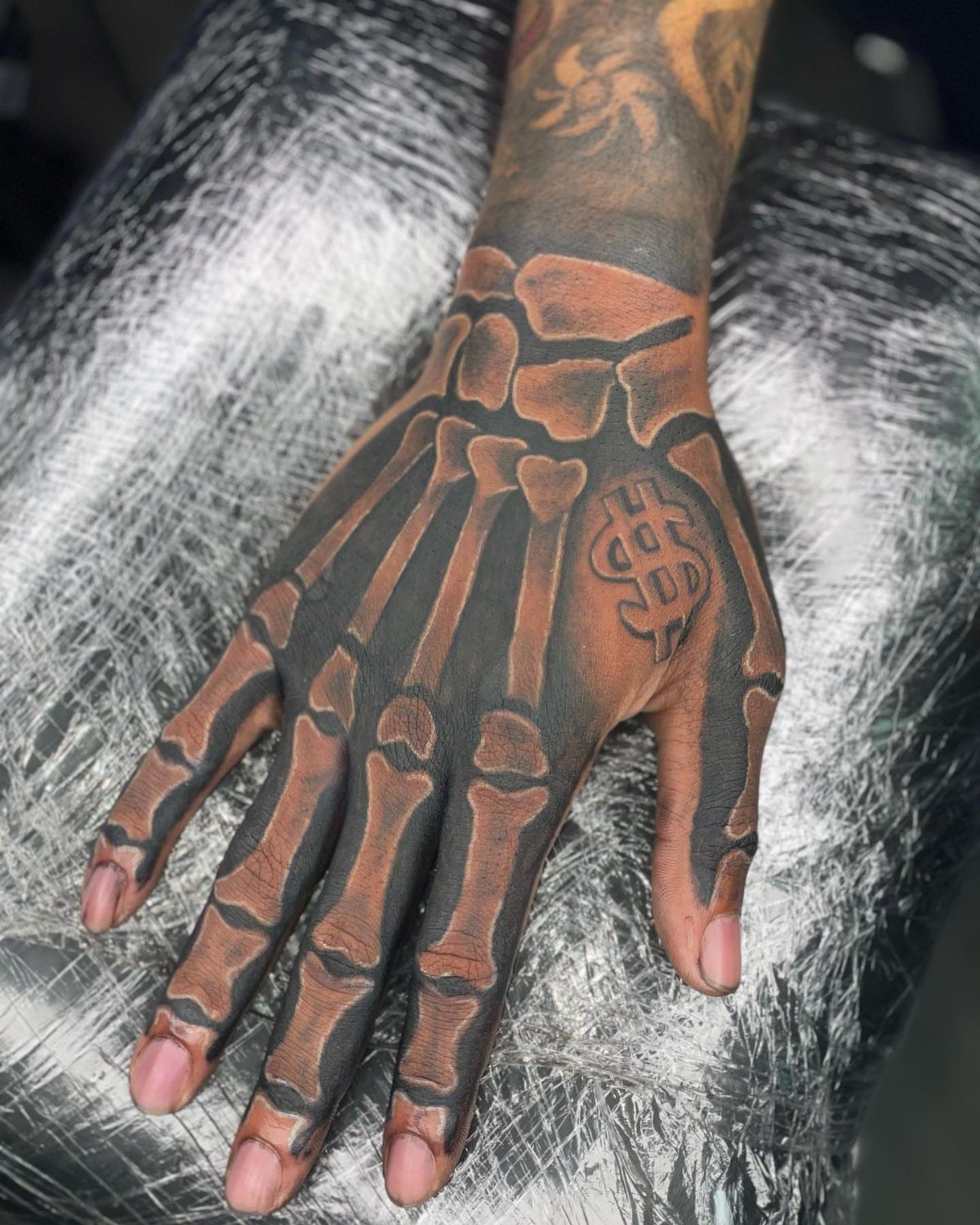 Skeleton bone tattoo on a hand with a dollar sign symbol on the side.