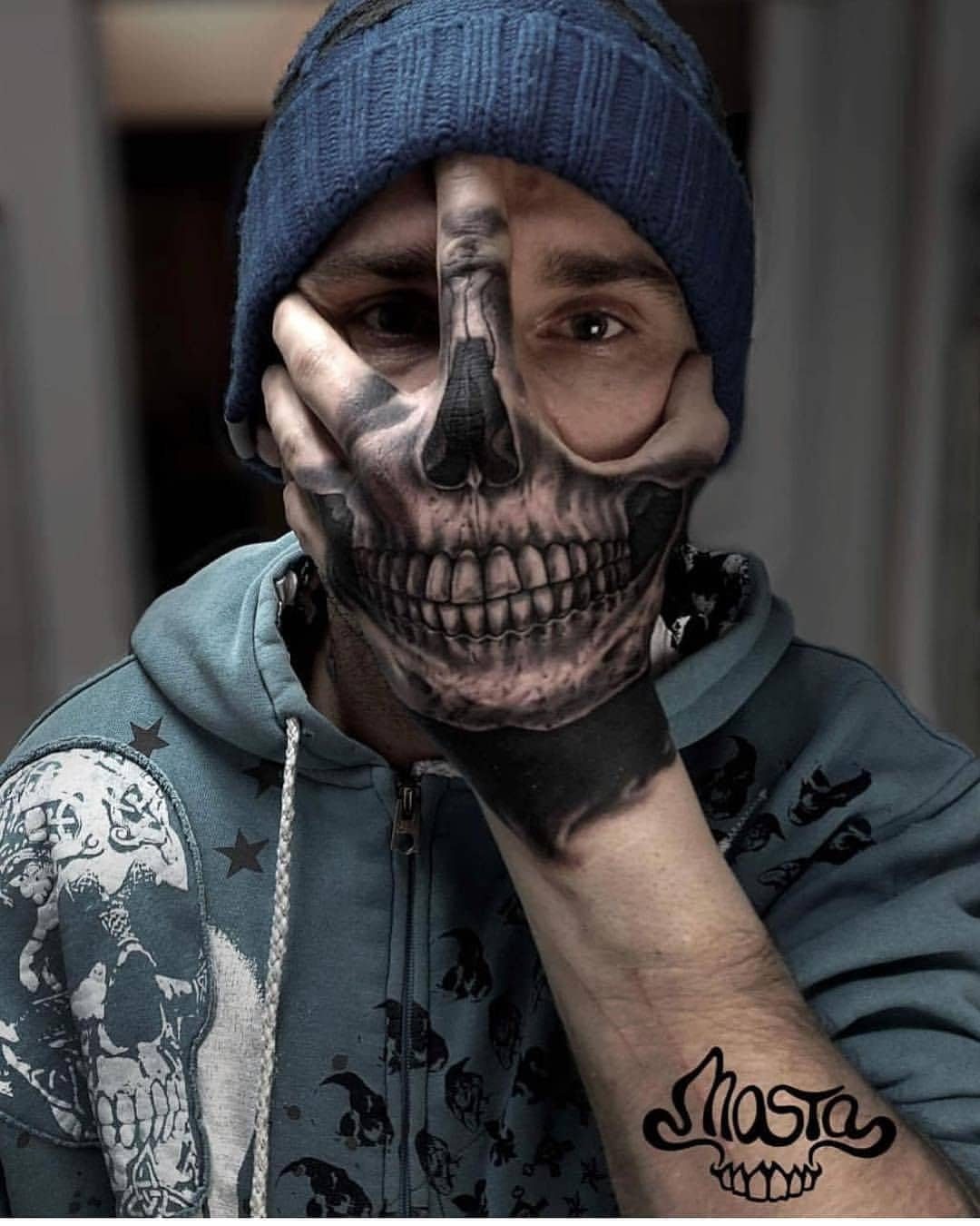 Man with a realistic skeleton face tattoo on his hand covering his mouth.