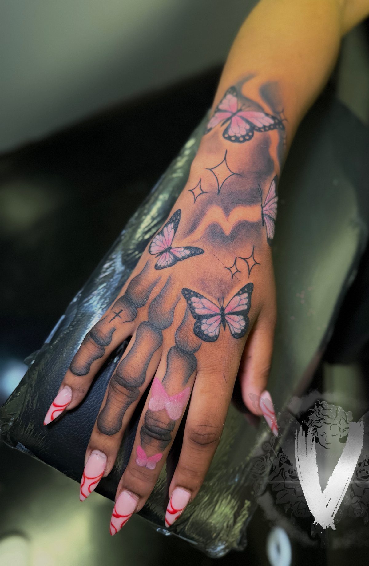 Skeleton hand tattoo on a person's hand adorned with several pink butterflies.