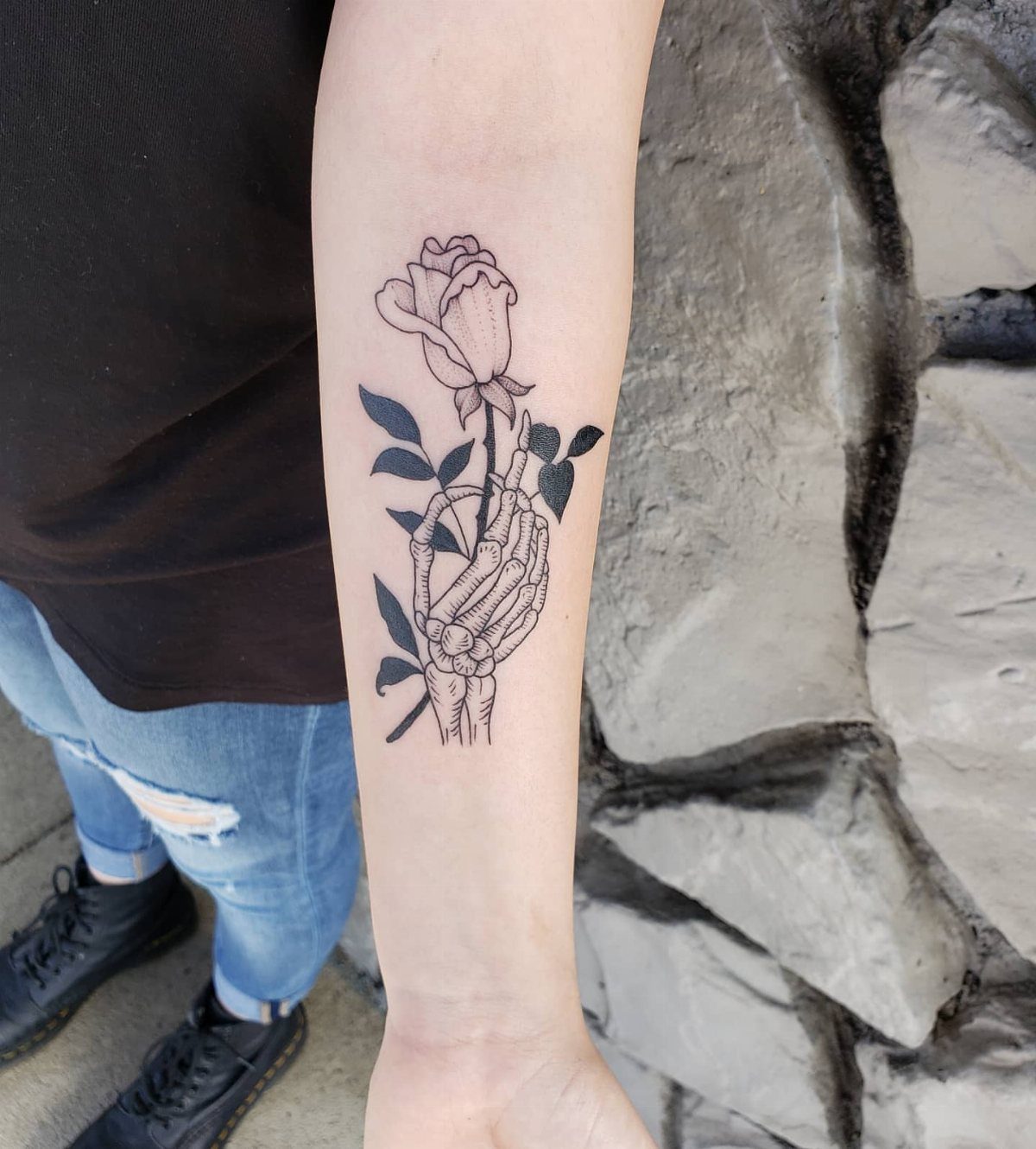 Skeleton hand holding a rose tattoo on a person's forearm.
