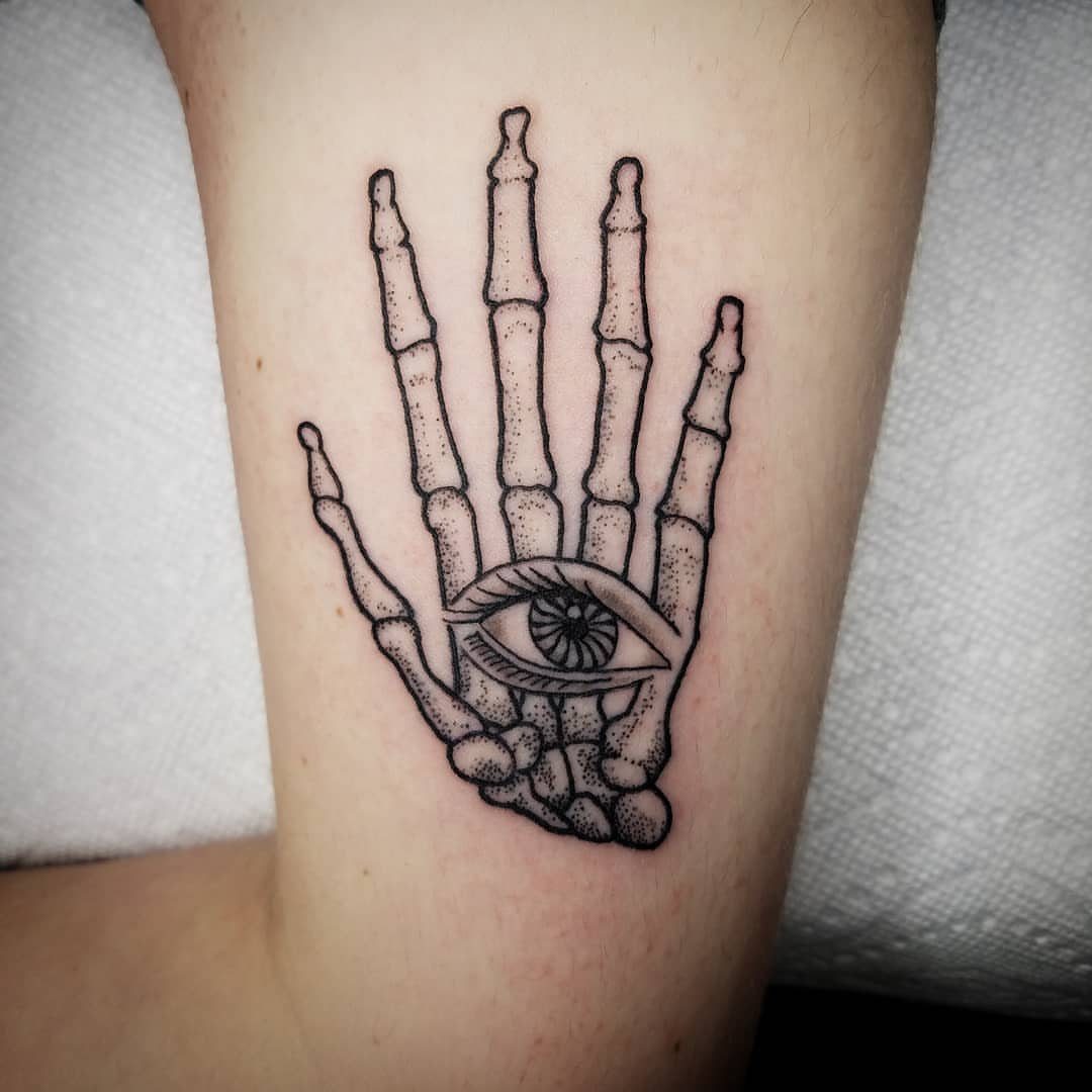 Skeleton hand tattoo with an eye in the palm on a person's arm.