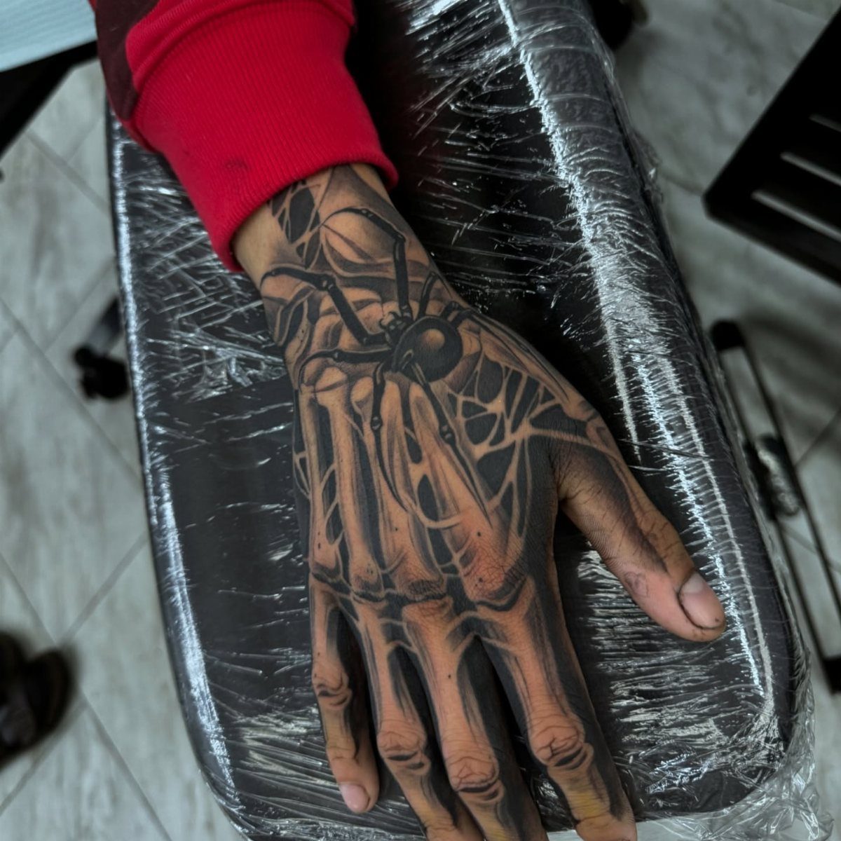 Skeleton hand tattoo with a large spider on the back of a hand.