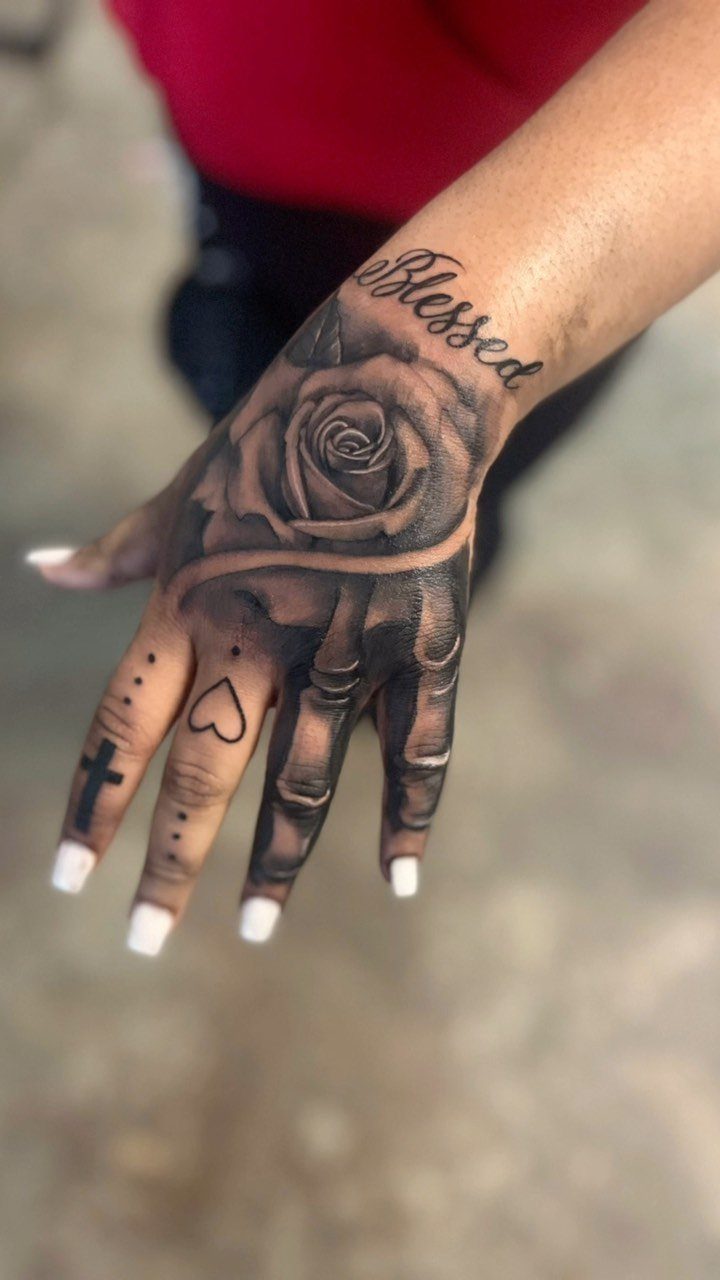 Hand tattoo featuring a large rose and skeletal finger bones in black and grey ink.