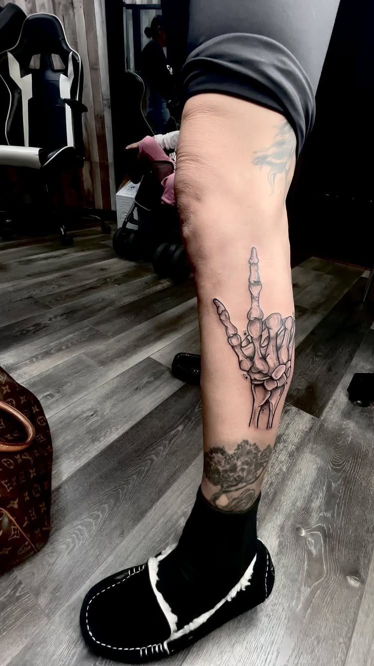 Skeleton hand tattoo on a person's lower leg with black and grey ink.