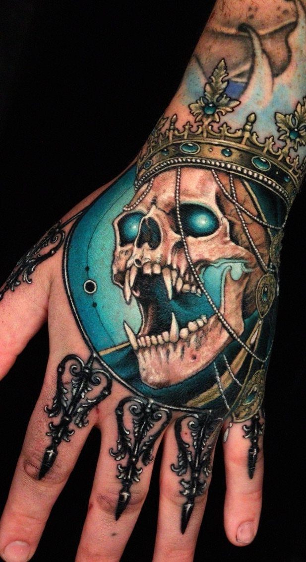 Skull tattoo on a hand featuring a golden crown and glowing blue eyes.