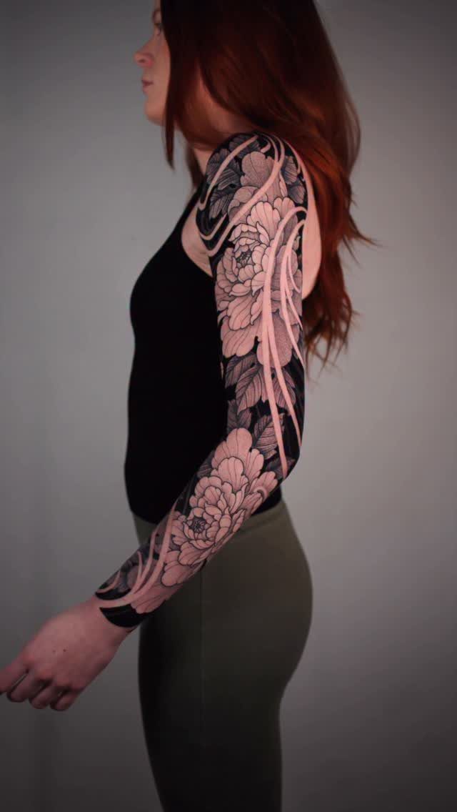 Woman with red hair showing a floral sleeve tattoo on her arm