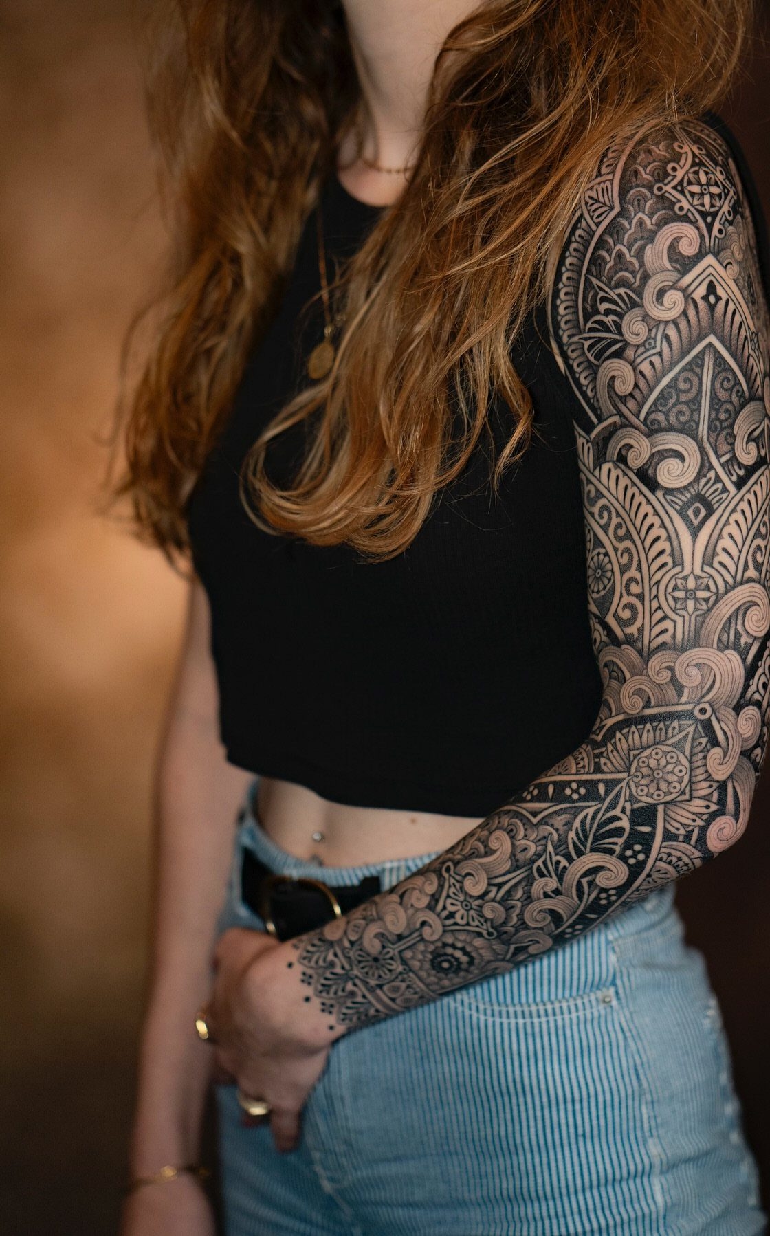 Woman with a full arm sleeve tattoo featuring intricate black ornamental geometric patterns.
