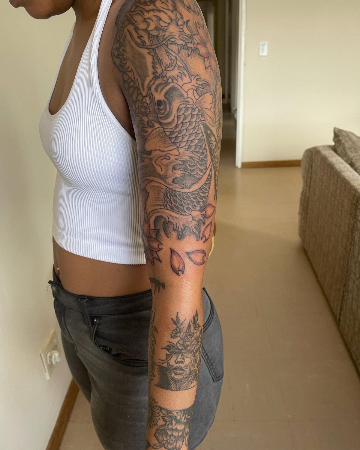 Woman's arm with a detailed sleeve tattoo featuring a koi fish and flowers.