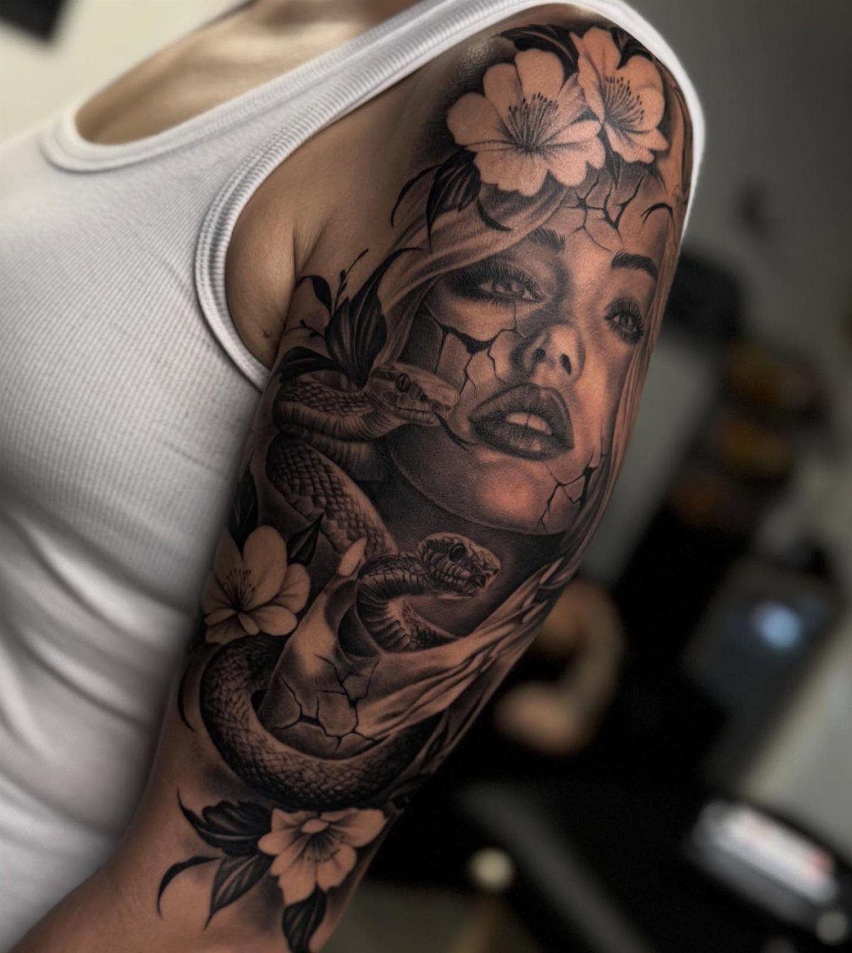 Sleeve tattoo featuring a woman's face, a snake, and flowers in black and grey.