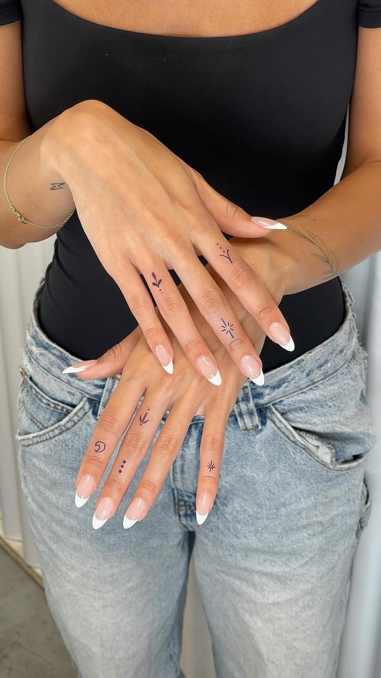 Hands with small minimalist black ink tattoos on the fingers and knuckles.