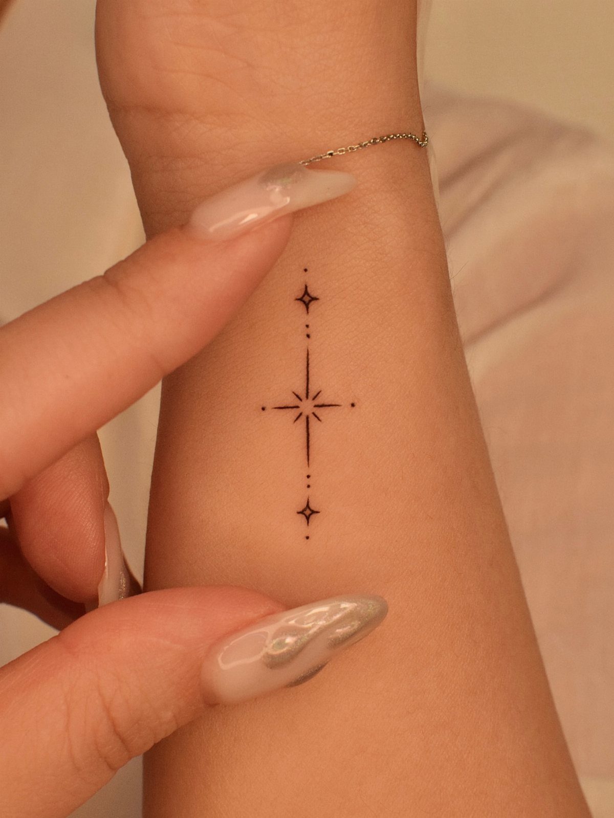 Small black star tattoo with a vertical line on a person's inner wrist