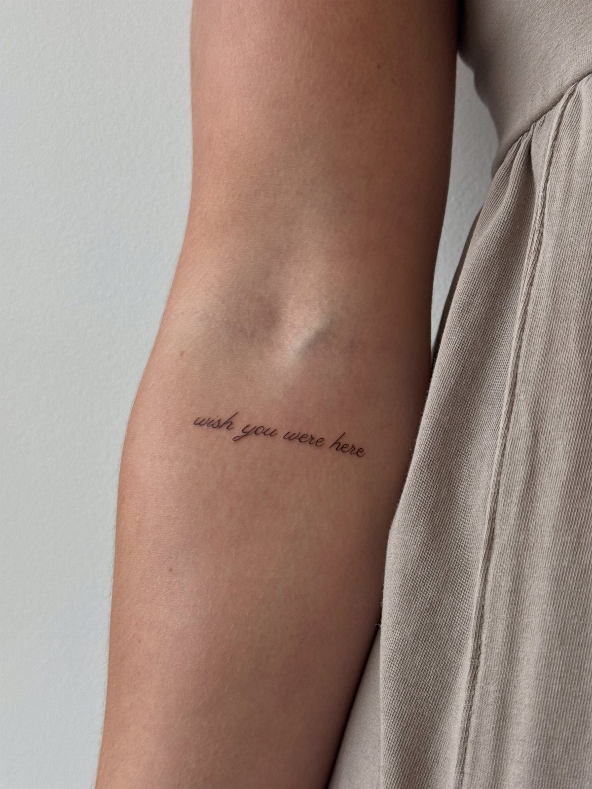 Cursive handwriting tattoo on a forearm reading wish you were here