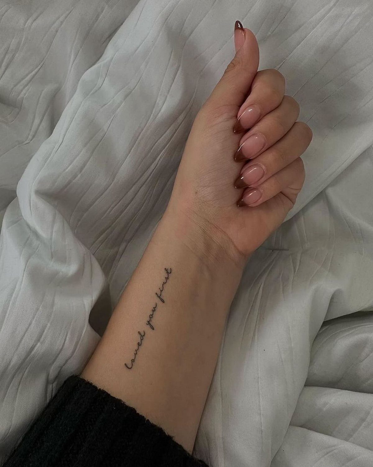 Cursive tattoo on a wrist reading loved you first resting on white fabric