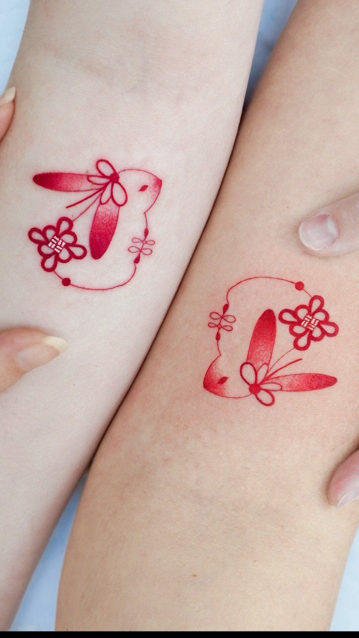 Two red bunny tattoos with flowers on the inner wrists of two people.