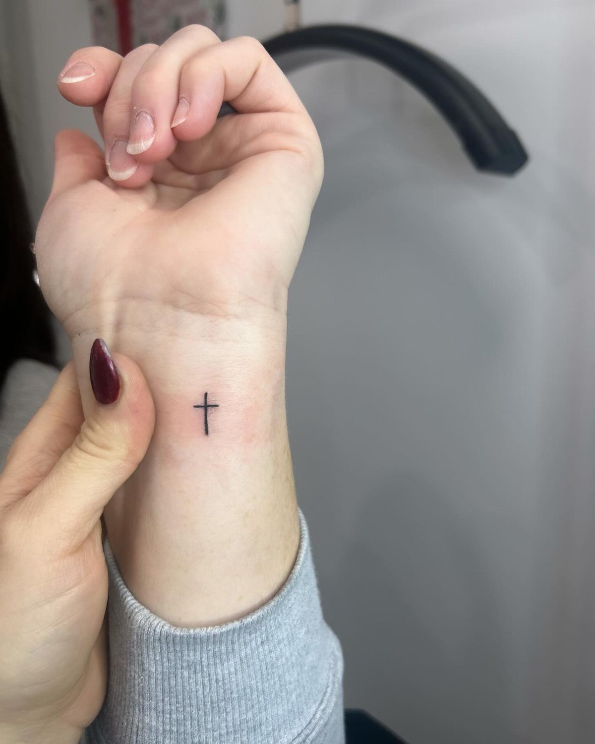 Small black cross tattoo on the inner wrist of a person.